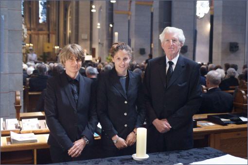 In der Gerricus-Kapelle von Vogt & Kamp Bestattungen Düsseldorf stehen drei Trauernde in Schwarz vor einer Kerze; Bestattung Düsseldorf.